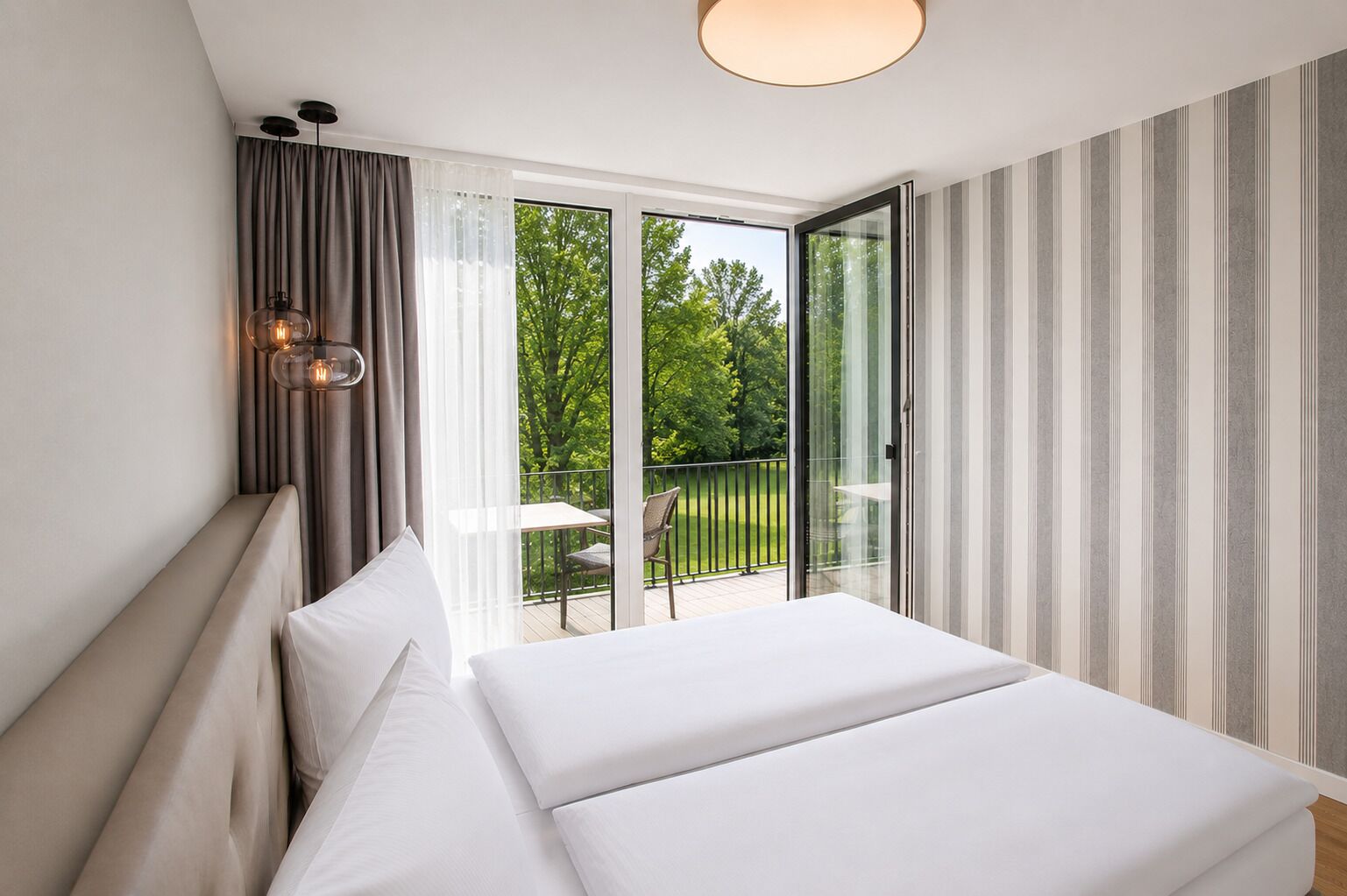 Une chambre à coucher avec un lit, des rideaux, une lampe et une vue sur un balcon aménagé avec du mobilier d’extérieur.