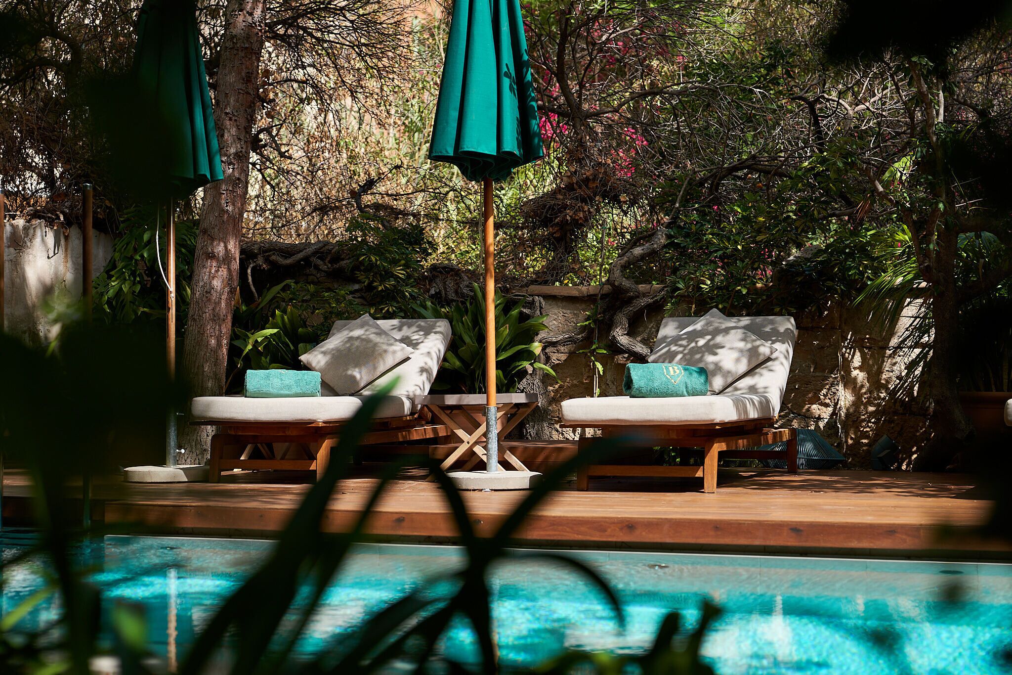 A poolside area with two lounge chairs, a wooden deck, and a stone wall in the background.