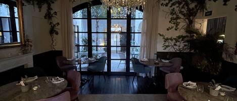 Un comedor con mesas y sillas redondas, una araña y vistas amplias a través de grandes ventanales.