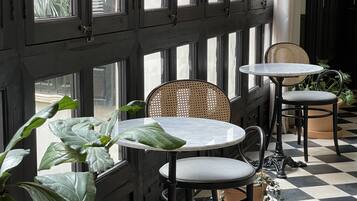 A room with a checkered floor, black and white walls, and a large window with multiple panes. There are two round tables with chairs, and a potted plant is visible.