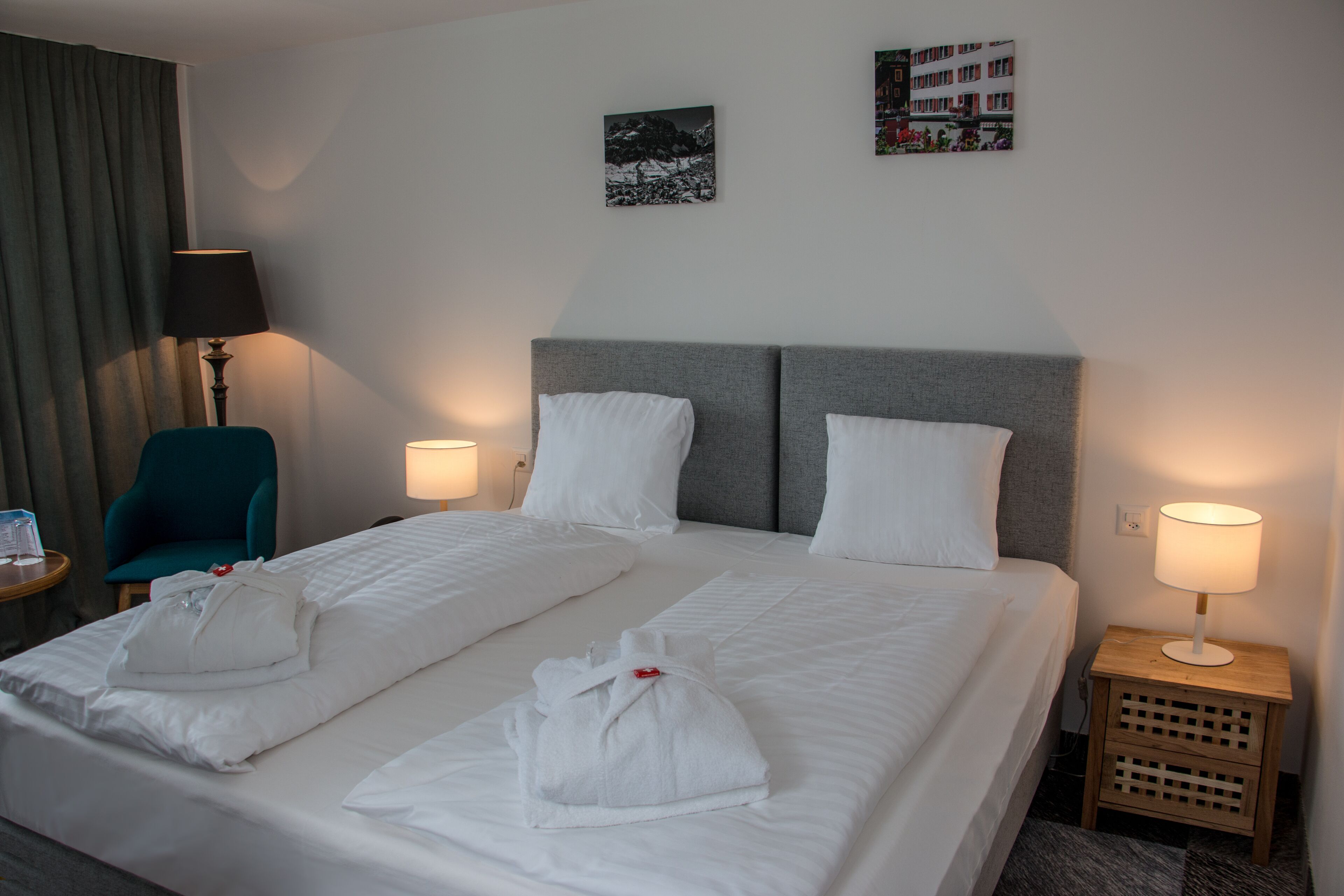 Ein Hotelzimmer mit einem Doppelbett, zwei Kissen, einem Nachttisch mit Lampe, einem Sessel und zwei Wandbildern.