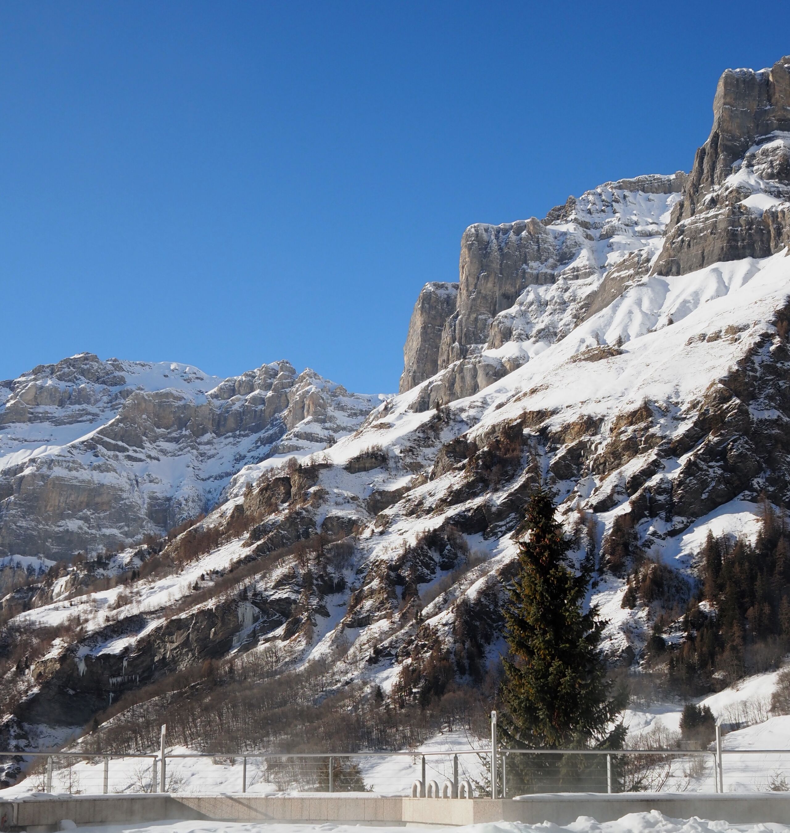 A mountainous landscape with snow-covered peaks and a clear blue sky.