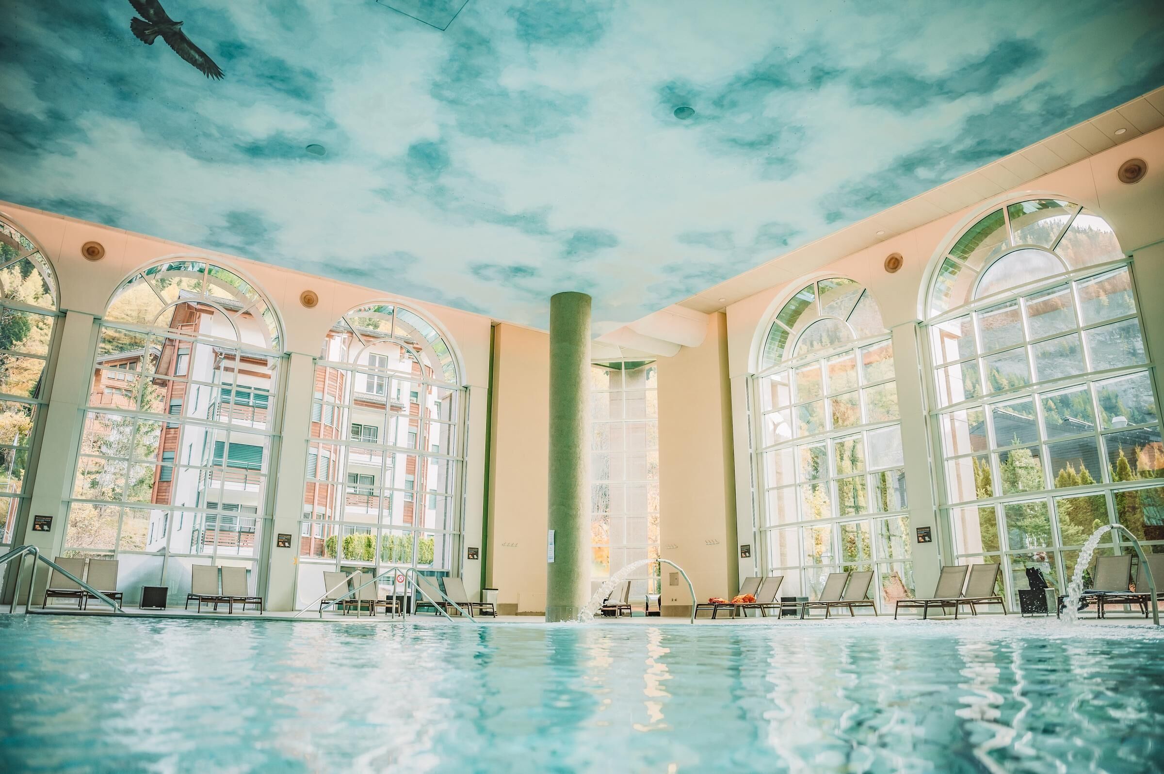 A swimming pool with lounge chairs and large arched windows.