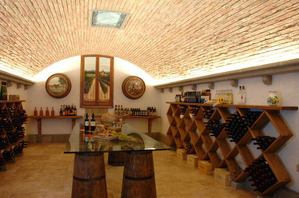 A wine cellar with wooden wine racks, a central table with bottles, and framed pictures on the walls.