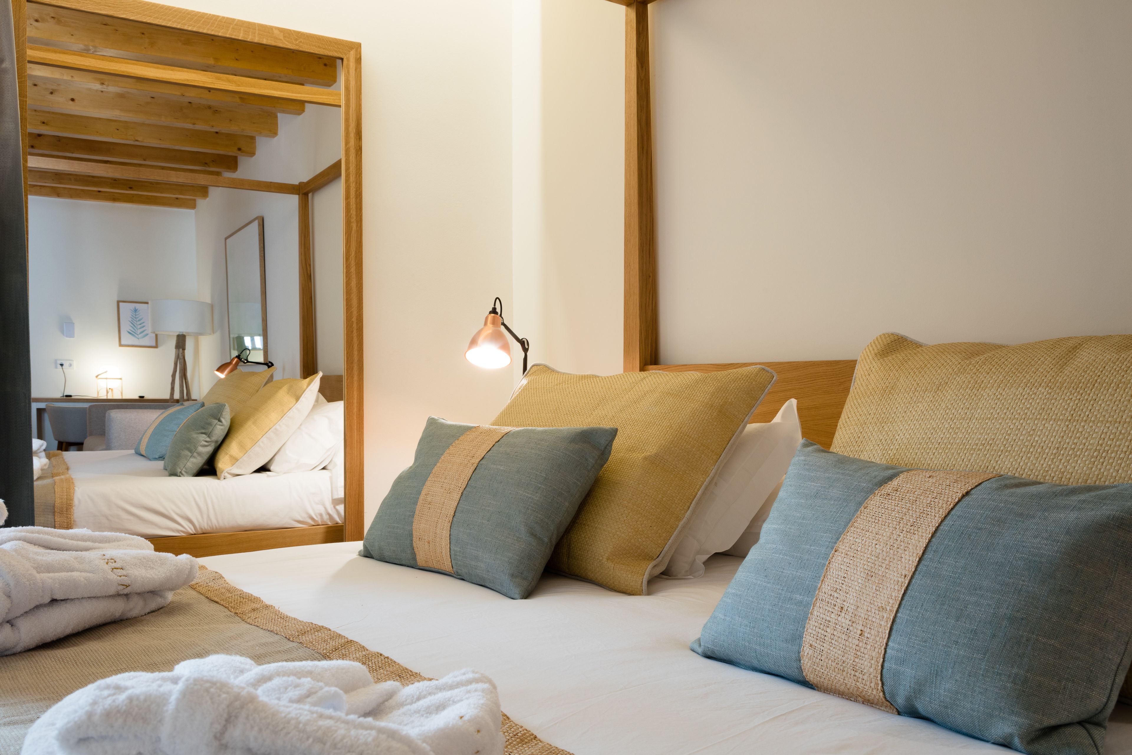 Habitación de hotel con techo de madera, una cama con varias almohadas, una lámpara de noche y un espejo.