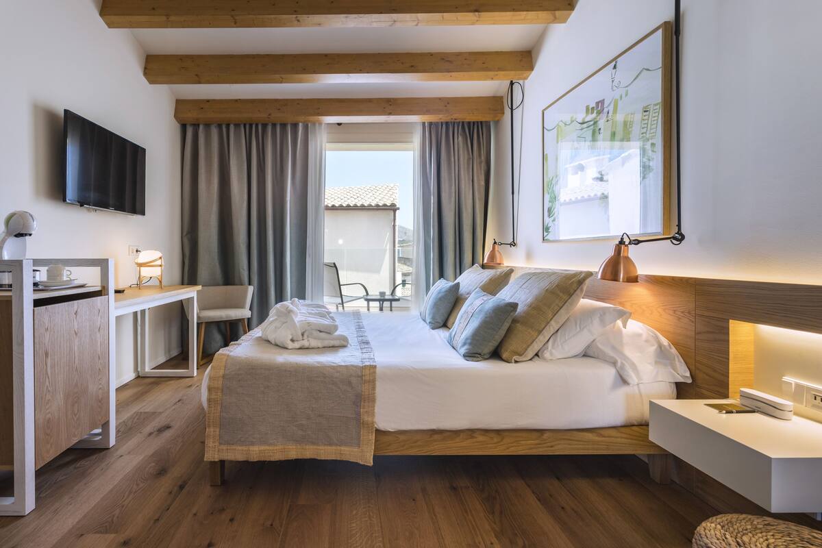 A modern hotel room with a wooden bed, a desk, a chair, a television, and a large window with curtains.