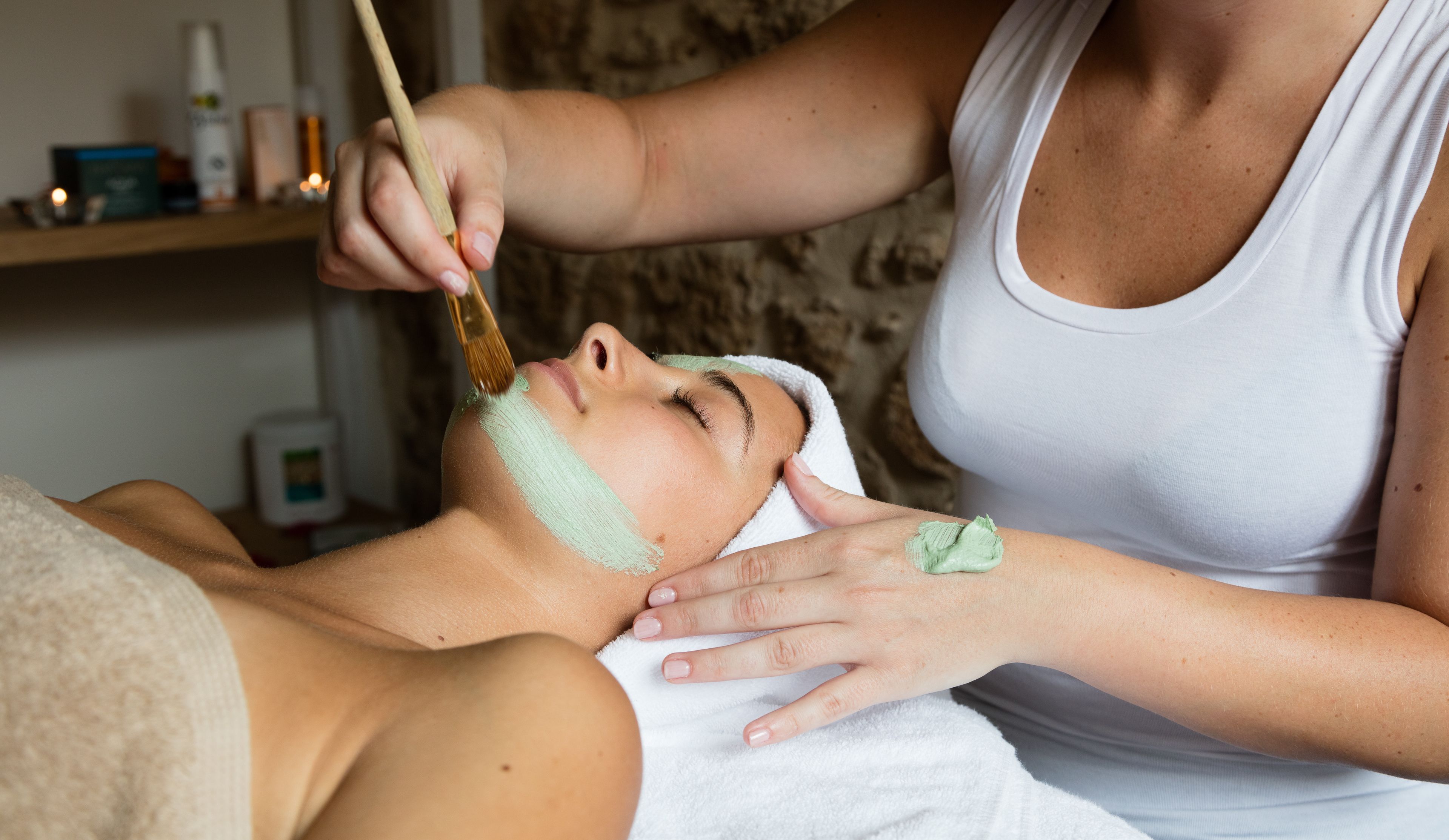 A person receiving a facial treatment with a brush and a green substance.