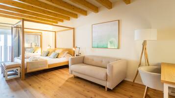 A modern bedroom with a wooden ceiling, a bed with a headboard, a beige sofa, a wooden table, and a chair.