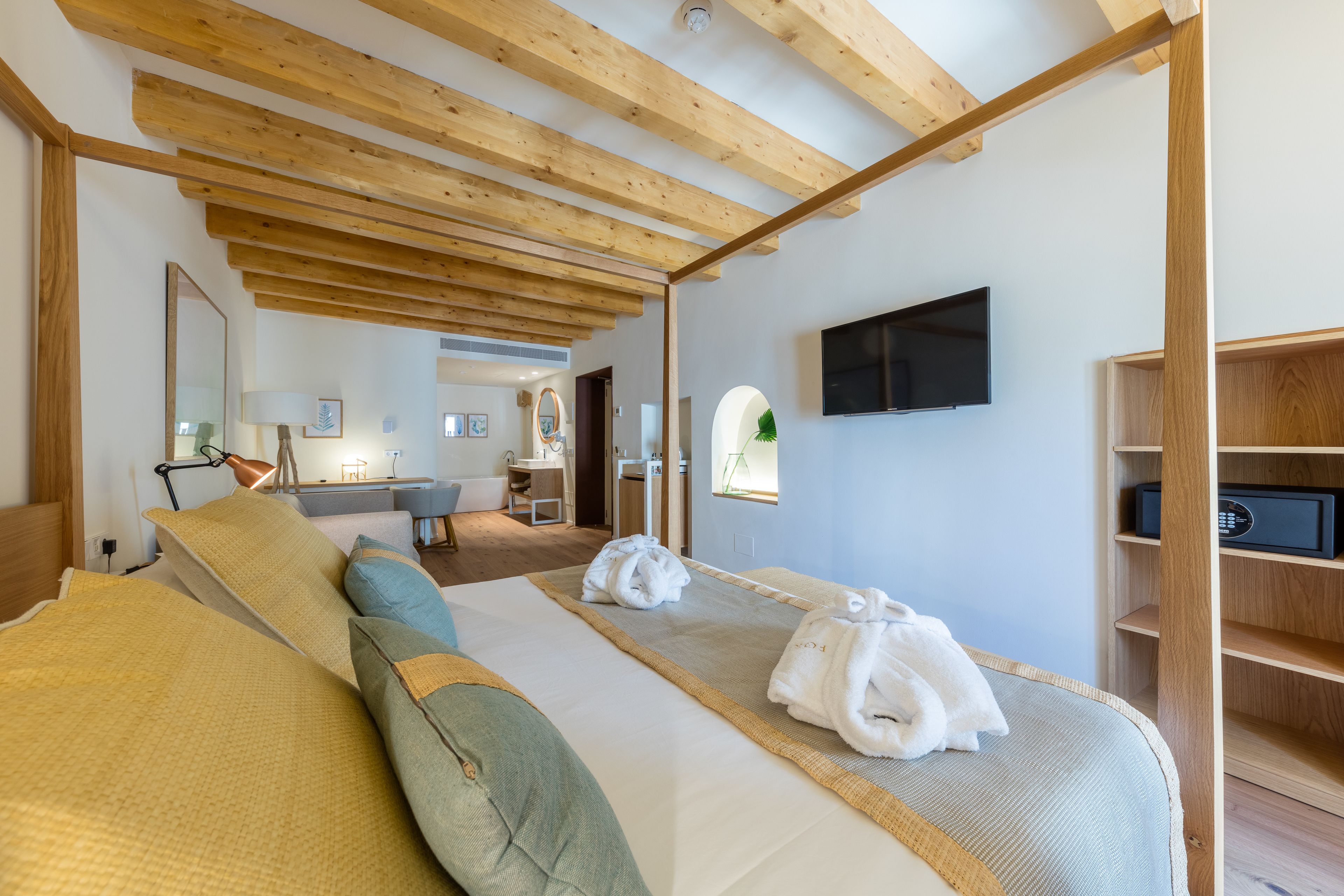 Une chambre d’hôtel moderne avec un plafond en bois, un grand lit recouvert d’une couette beige et verte, un téléviseur à écran plat et une étagère en bois.