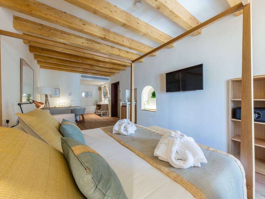 Une chambre d’hôtel moderne avec un plafond en bois, un grand lit recouvert d’une couette beige et verte, un téléviseur à écran plat et une étagère en bois.
