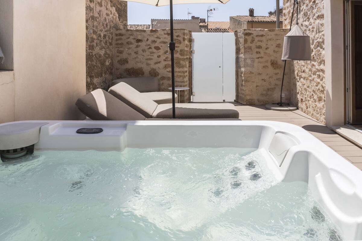 A hot tub with a stone wall backdrop, a lounge chair, and a small table.