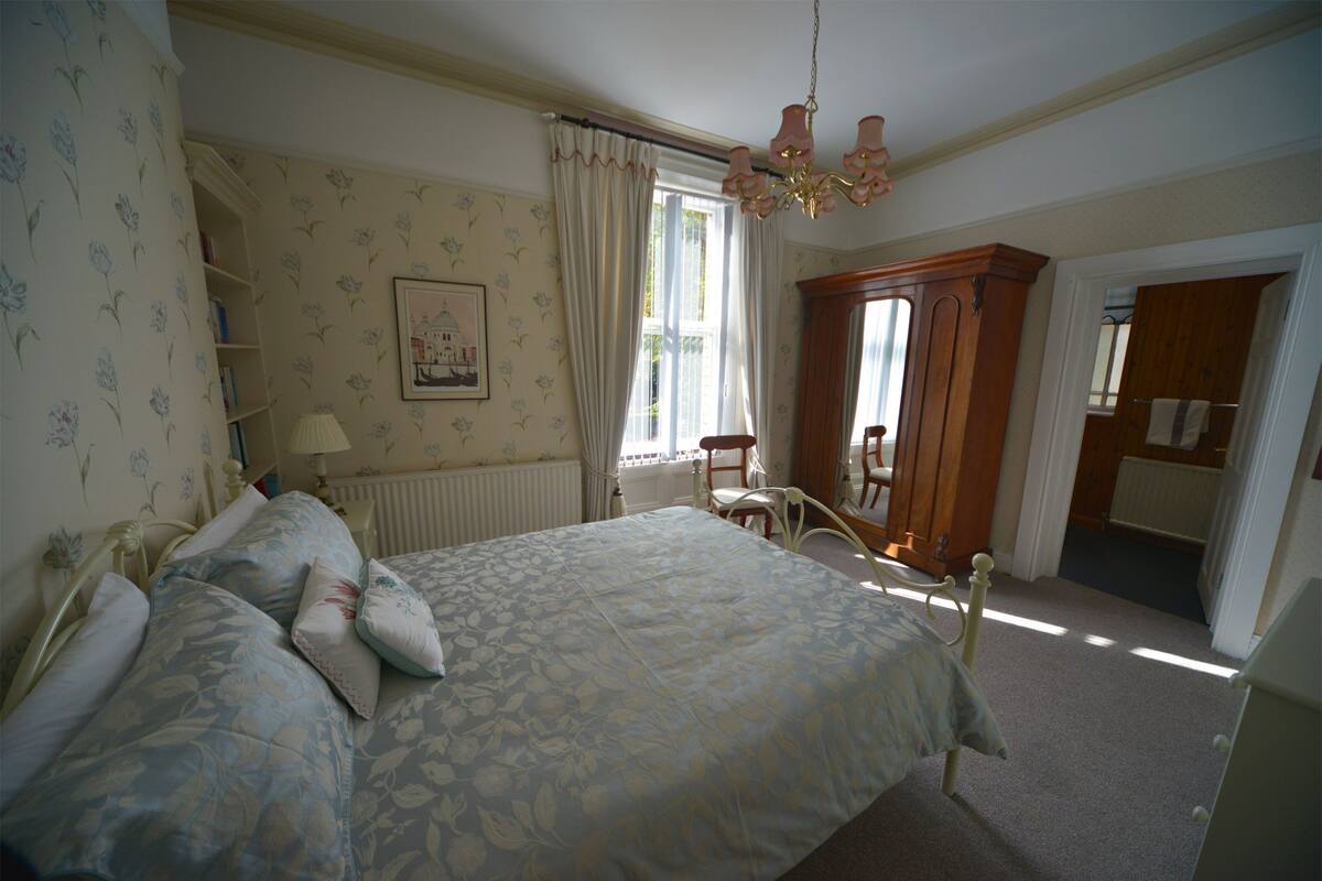 A bedroom with a large bed, a wooden wardrobe, a chair, and a radiator.