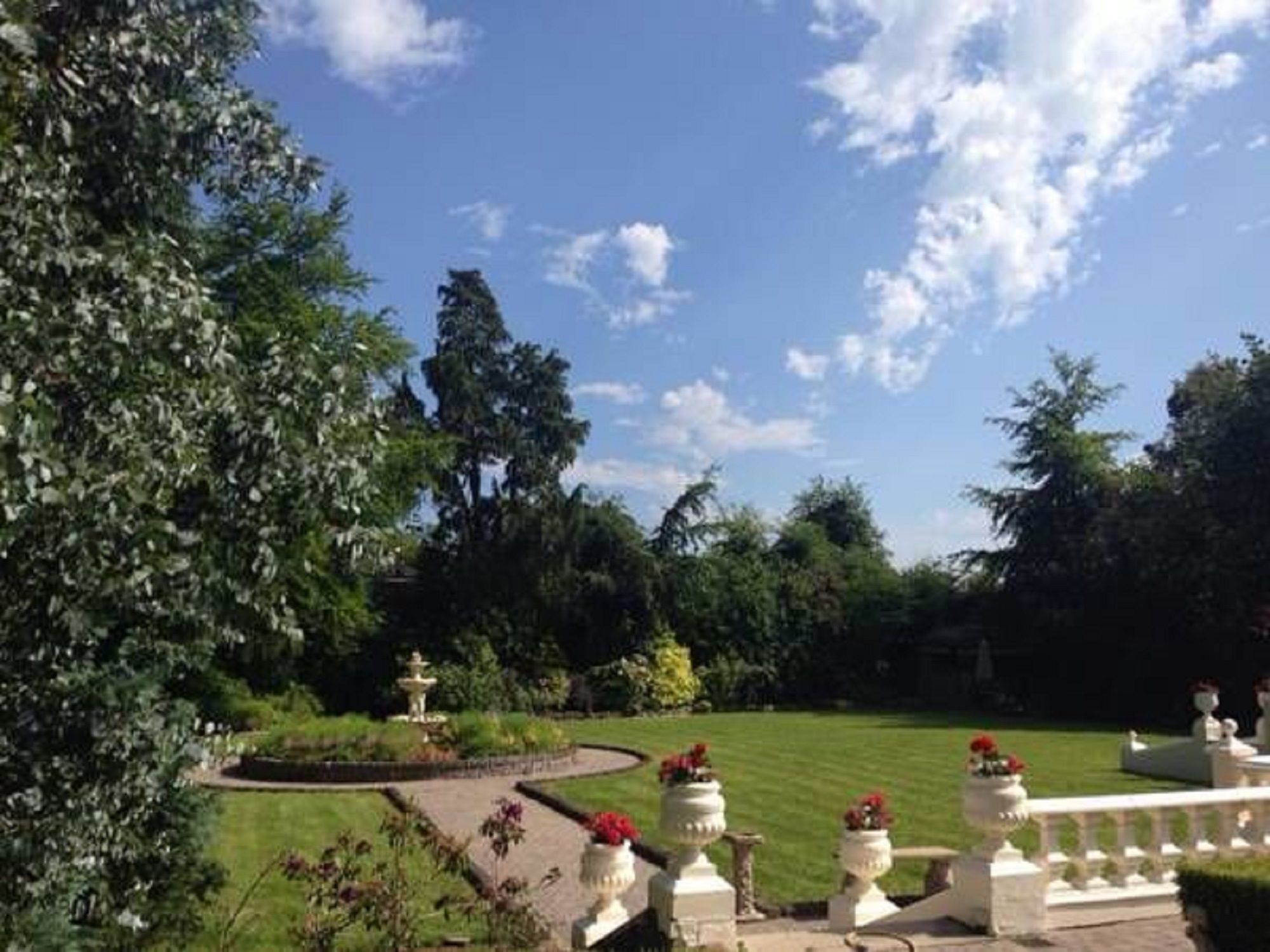 A garden with a fountain, white urns with flowers, and a white fence.