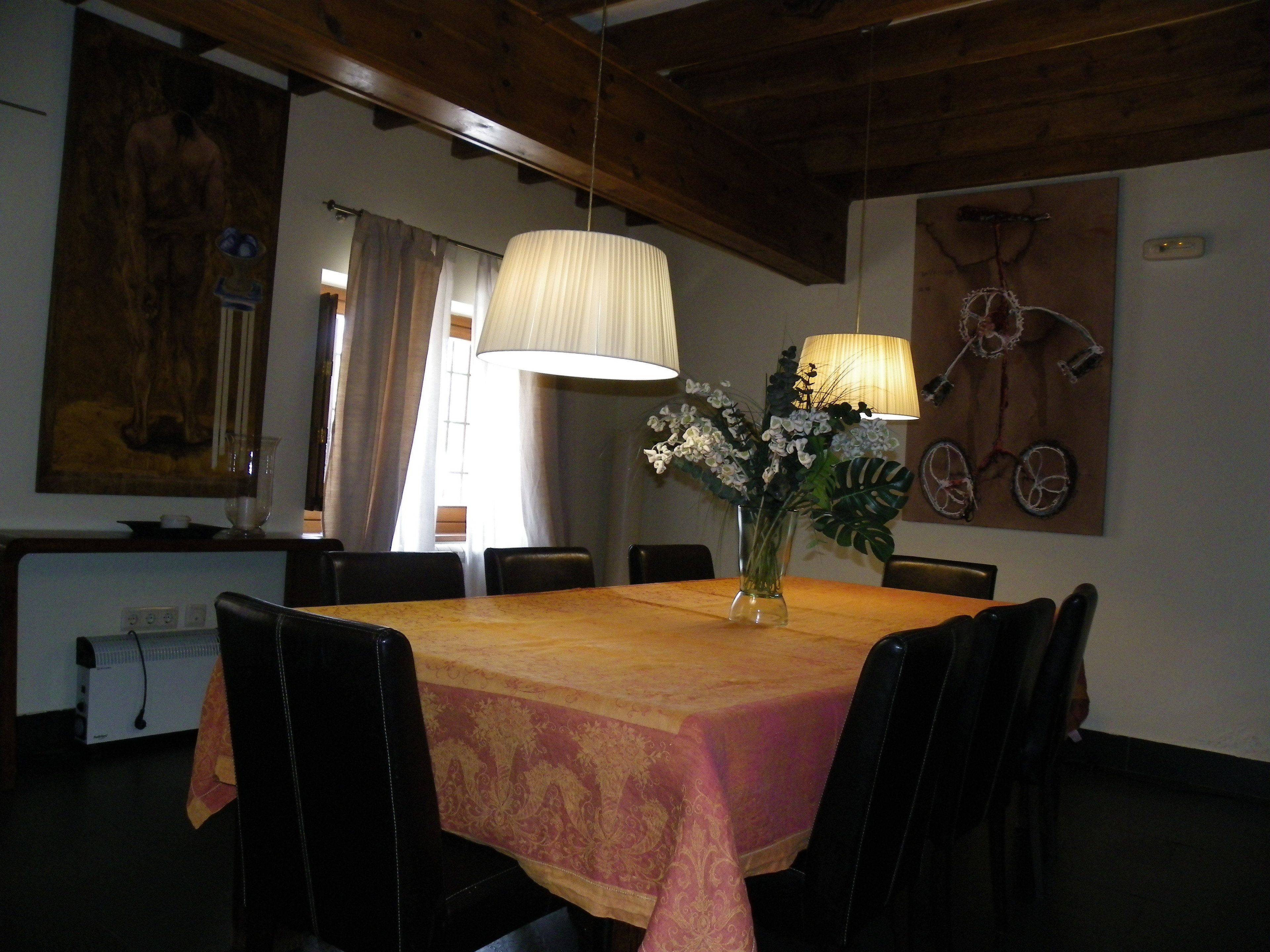 Un comedor con una mesa de madera, sillas negras, un florero con flores y una obra de arte con una bicicleta colgada en la pared.