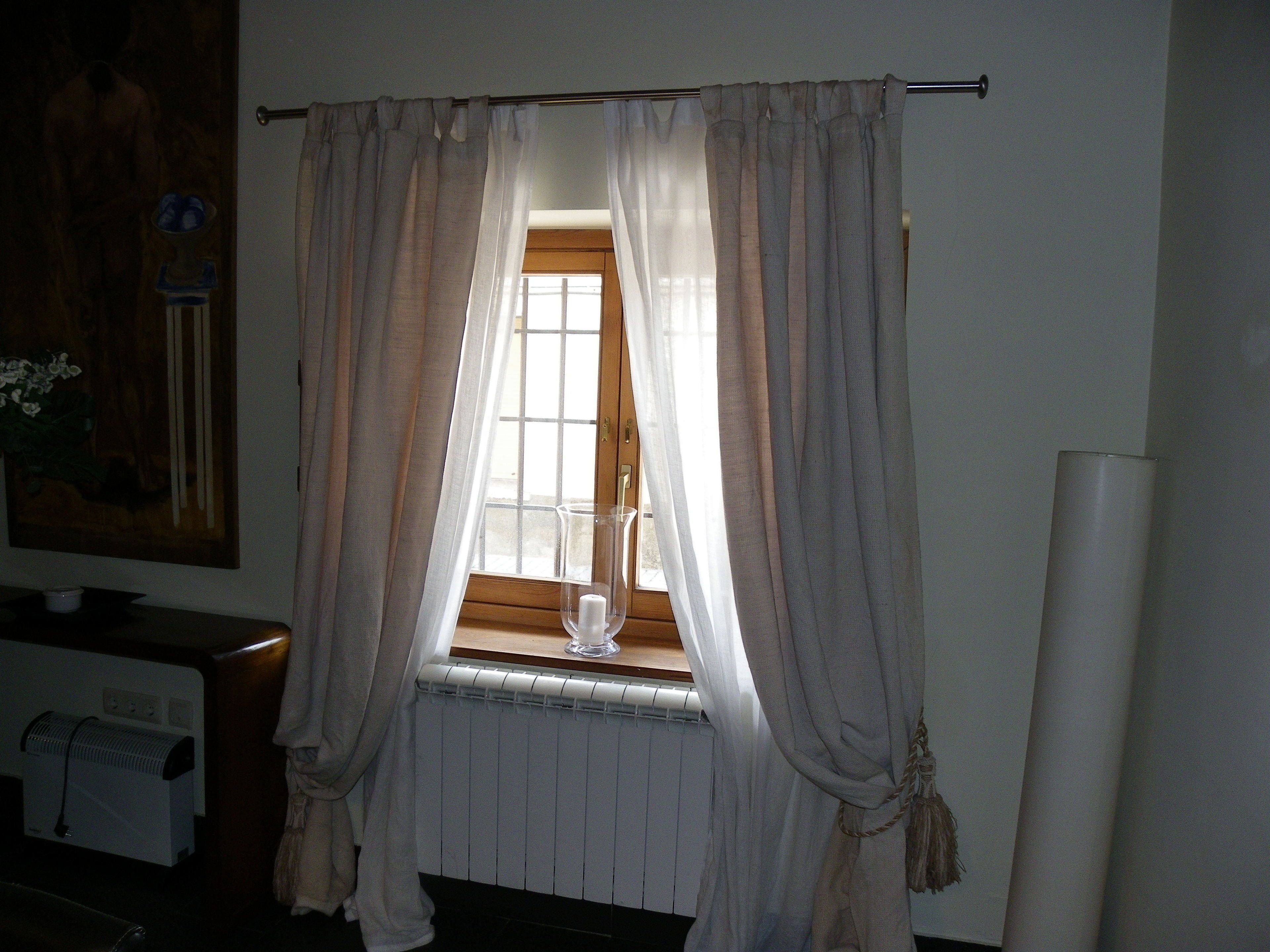 A room with a window covered by sheer curtains, a radiator below, and a painting on the wall.