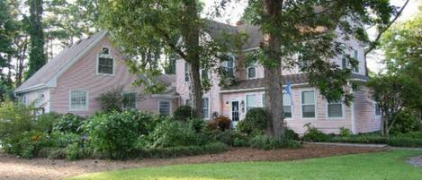 A two-story house with a sloped roof, surrounded by lush greenery and a well-maintained lawn.