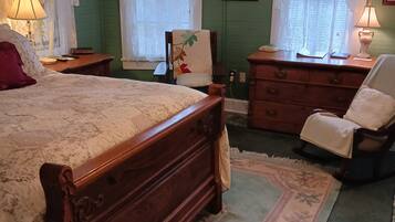 A bedroom with a wooden bed, two nightstands, a chair, a dresser, and a window with lace curtains.