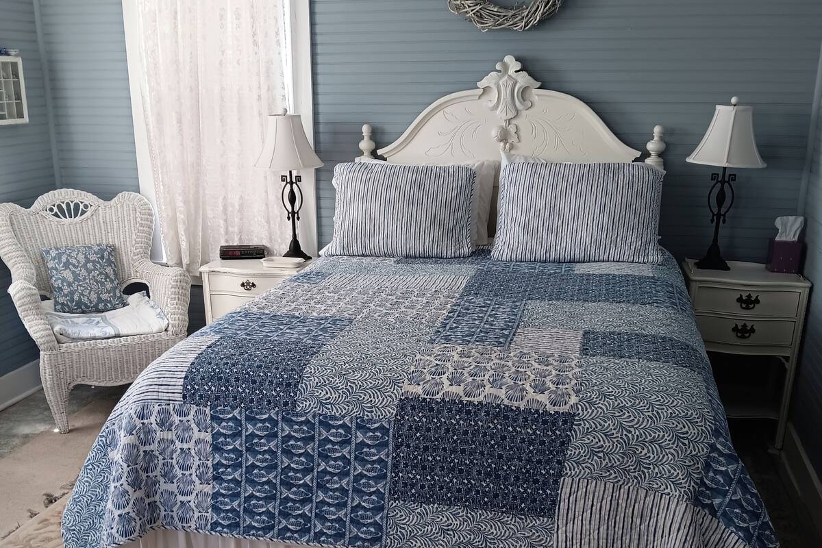 A bedroom with a bed, a chair, a nightstand, a lamp, and a wall decoration.