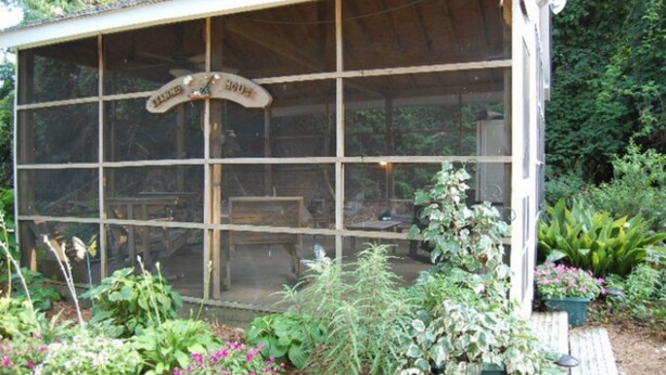 A conservatory with a wooden frame and glass panels, surrounded by various plants and flowers. - Island House of Wanchese (Wanchese)