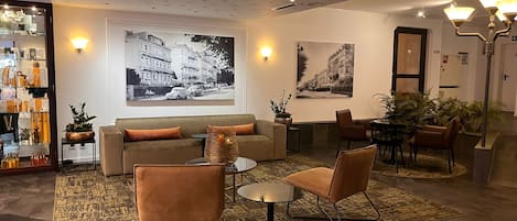 Una sala de estar moderna con un sofá, dos sillones, una mesa de centro y un comedor con mesa y sillas. Hay dos fotografías grandes en blanco y negro en las paredes, una lámpara de pie y una pequeña mesa con una planta.