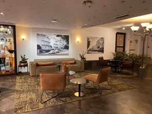 A modern living room with a sofa, two armchairs, a coffee table, and a dining area with a table and chairs. There are two large black and white photographs on the walls, a floor lamp, and a small table with a plant. - Parkhotel Bad Homburg (Bad Homburg v.d. Hoehe)