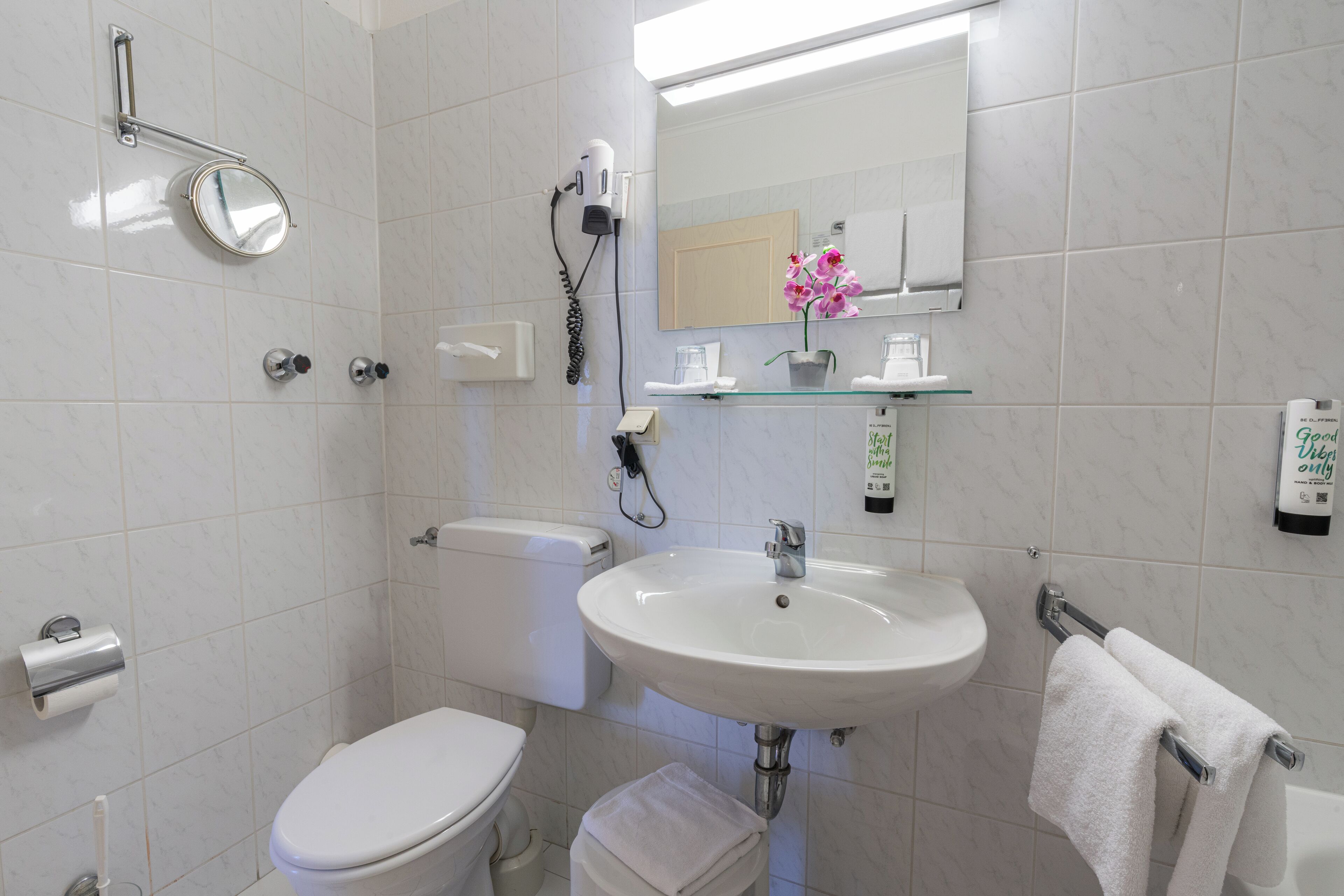 A bathroom with a toilet, sink, mirror, towel rack, and a hairdryer.