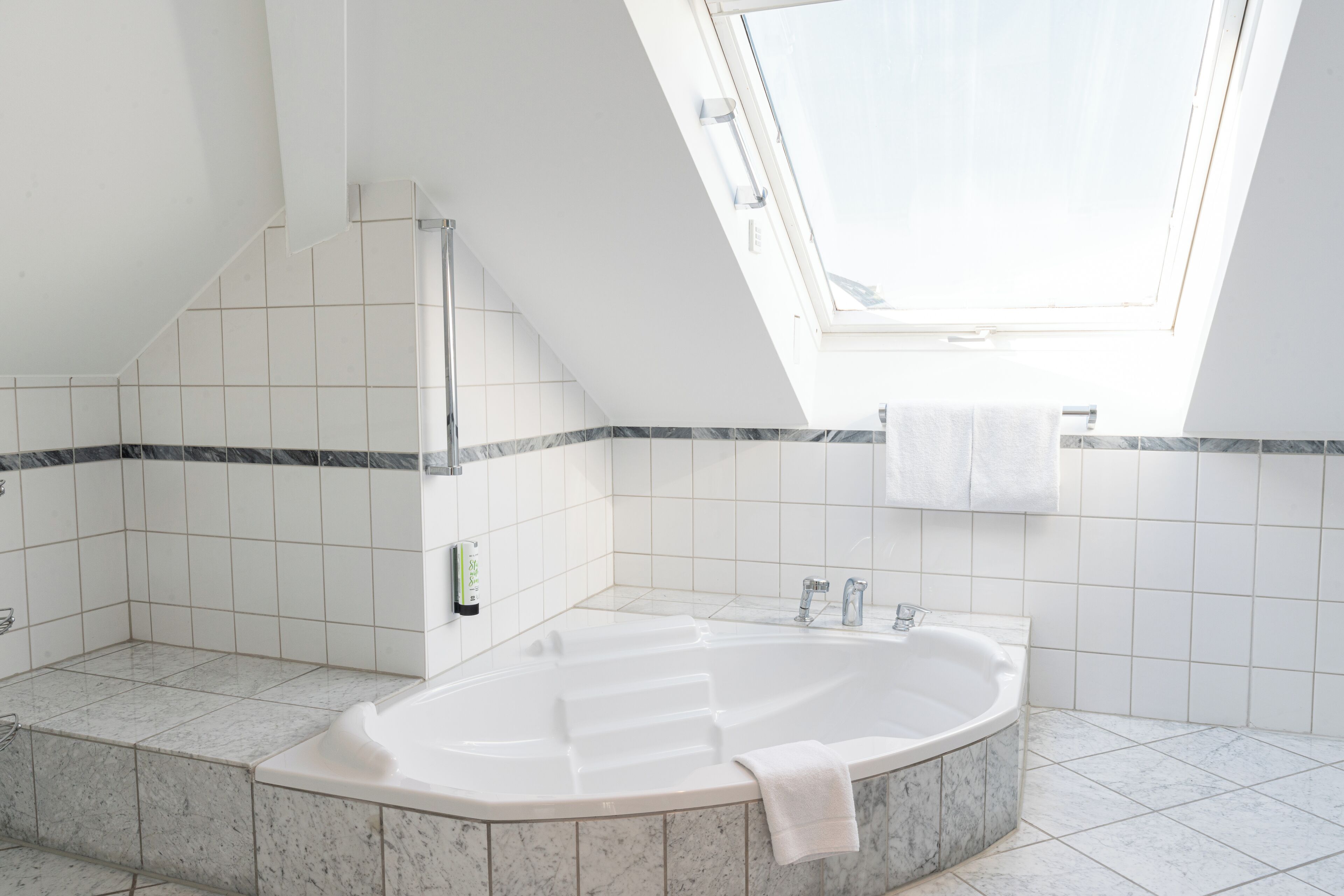 Een moderne badkamer met een vrijstaand bad, een dakraam en een betegelde vloer.