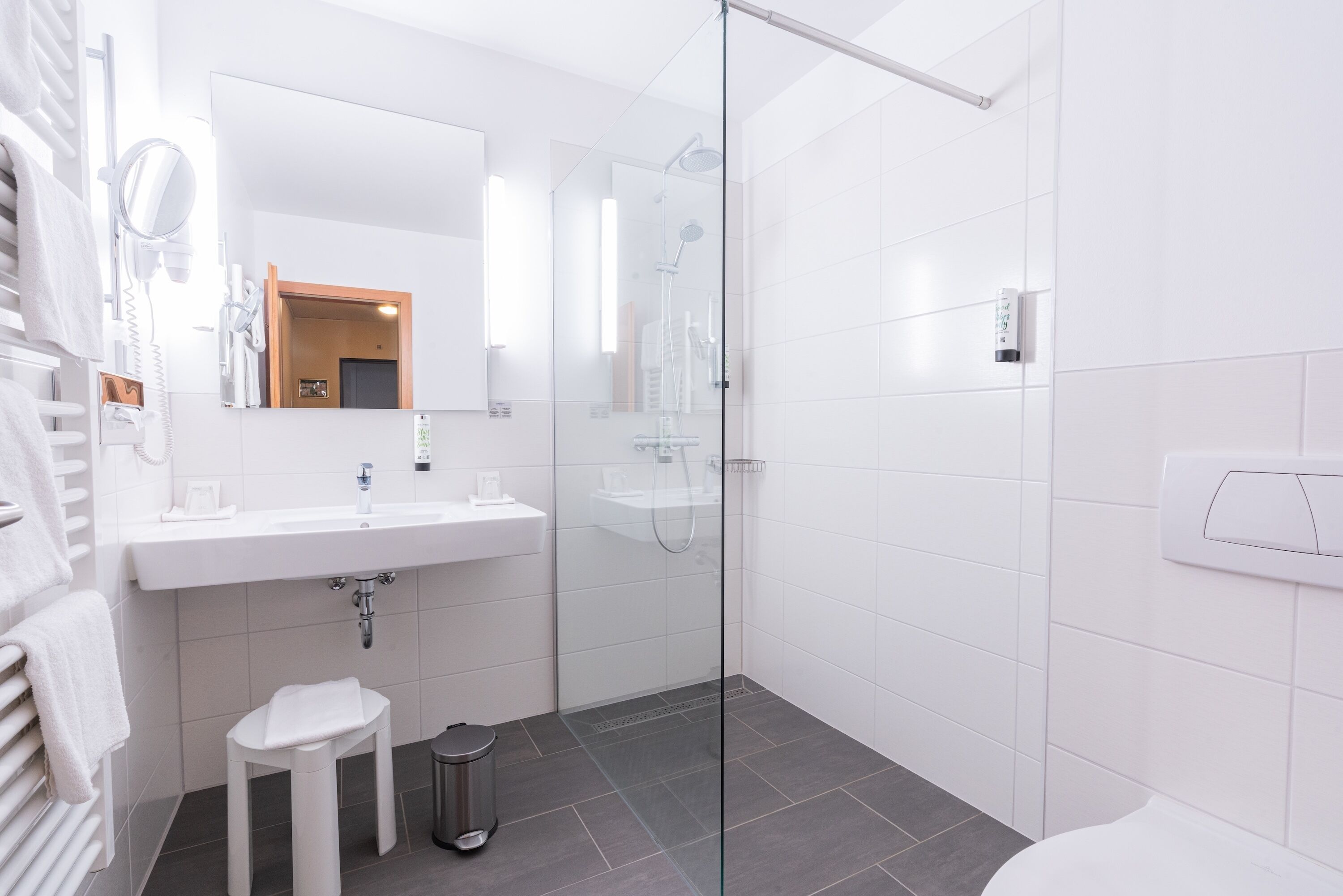 Une salle de bain moderne avec une douche à parois de verre, un lavabo blanc et un petit tabouret.