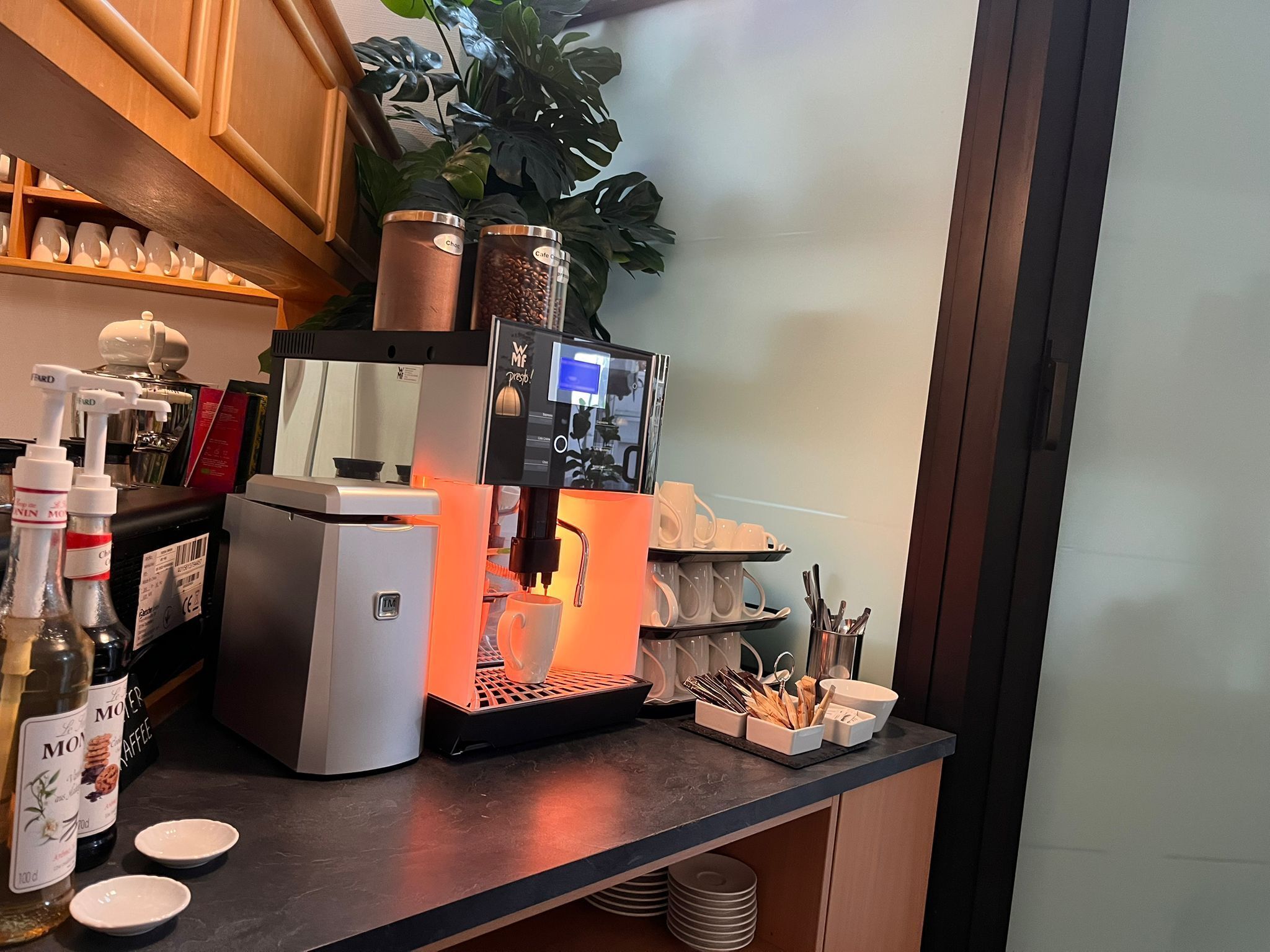 A coffee station with a coffee machine, cups, and a plant.