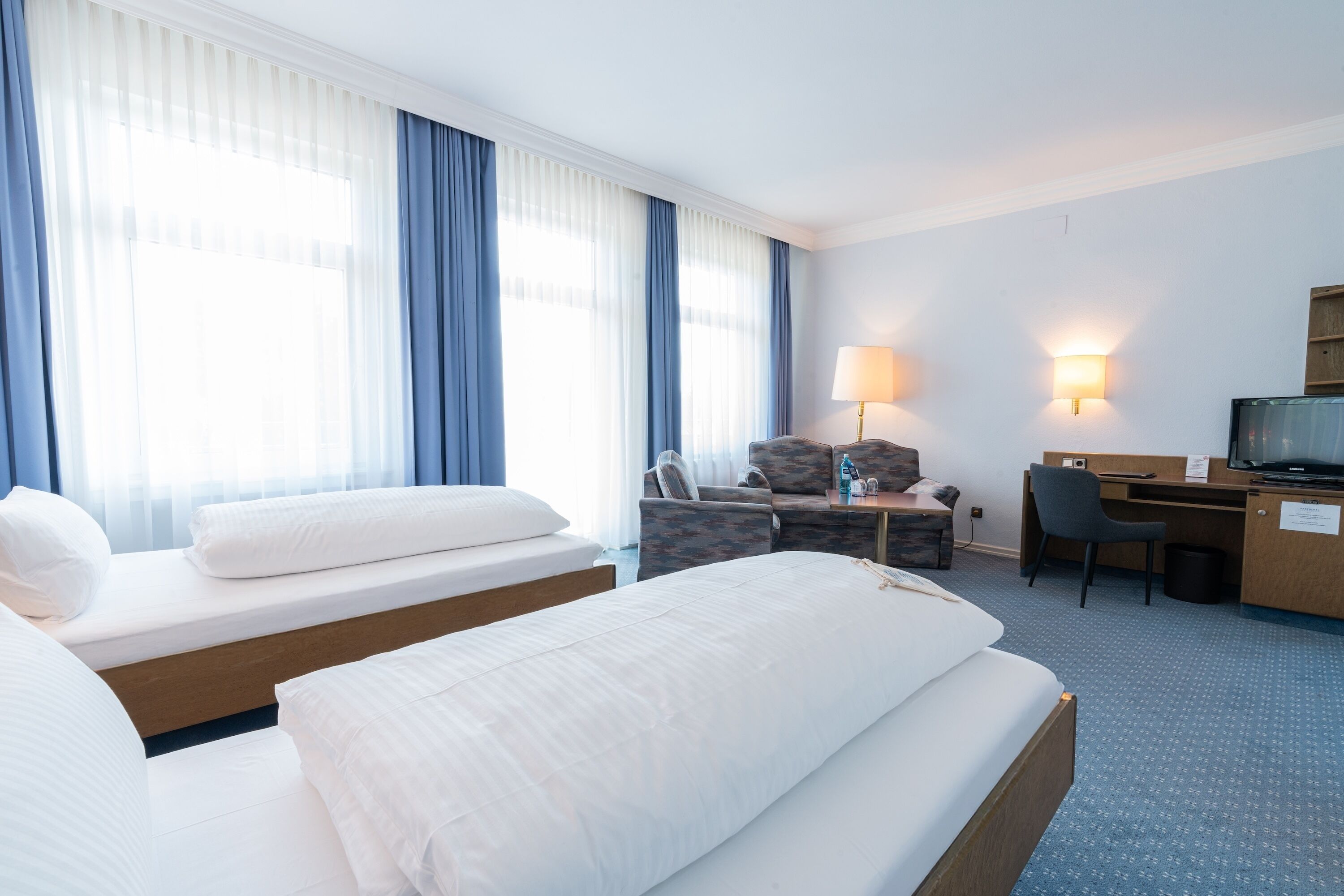 Habitación de hotel con dos camas, un escritorio, una silla, un televisor y dos lámparas fijadas a la pared.