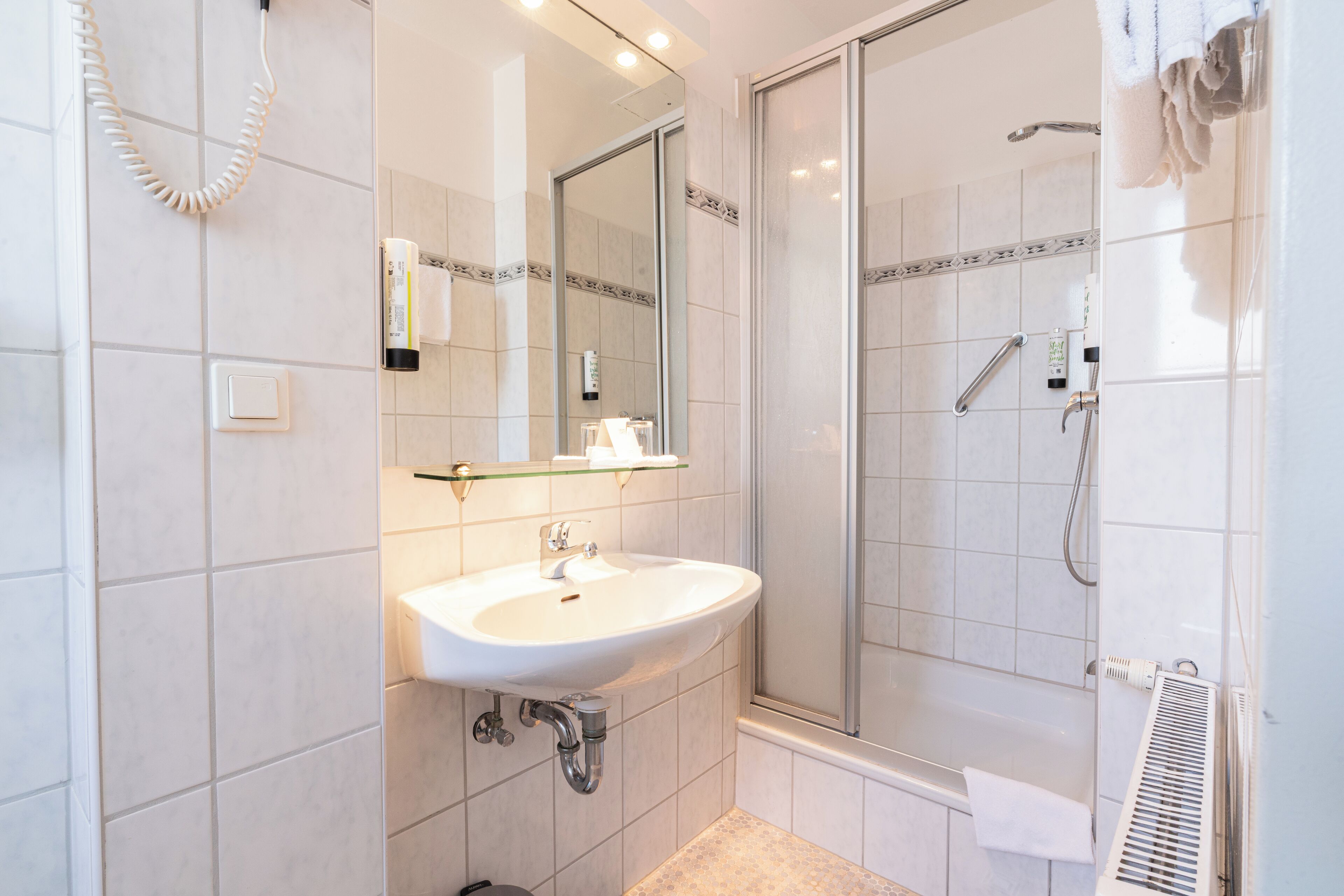A bathroom with a sink, mirror, shower, and towel rack.