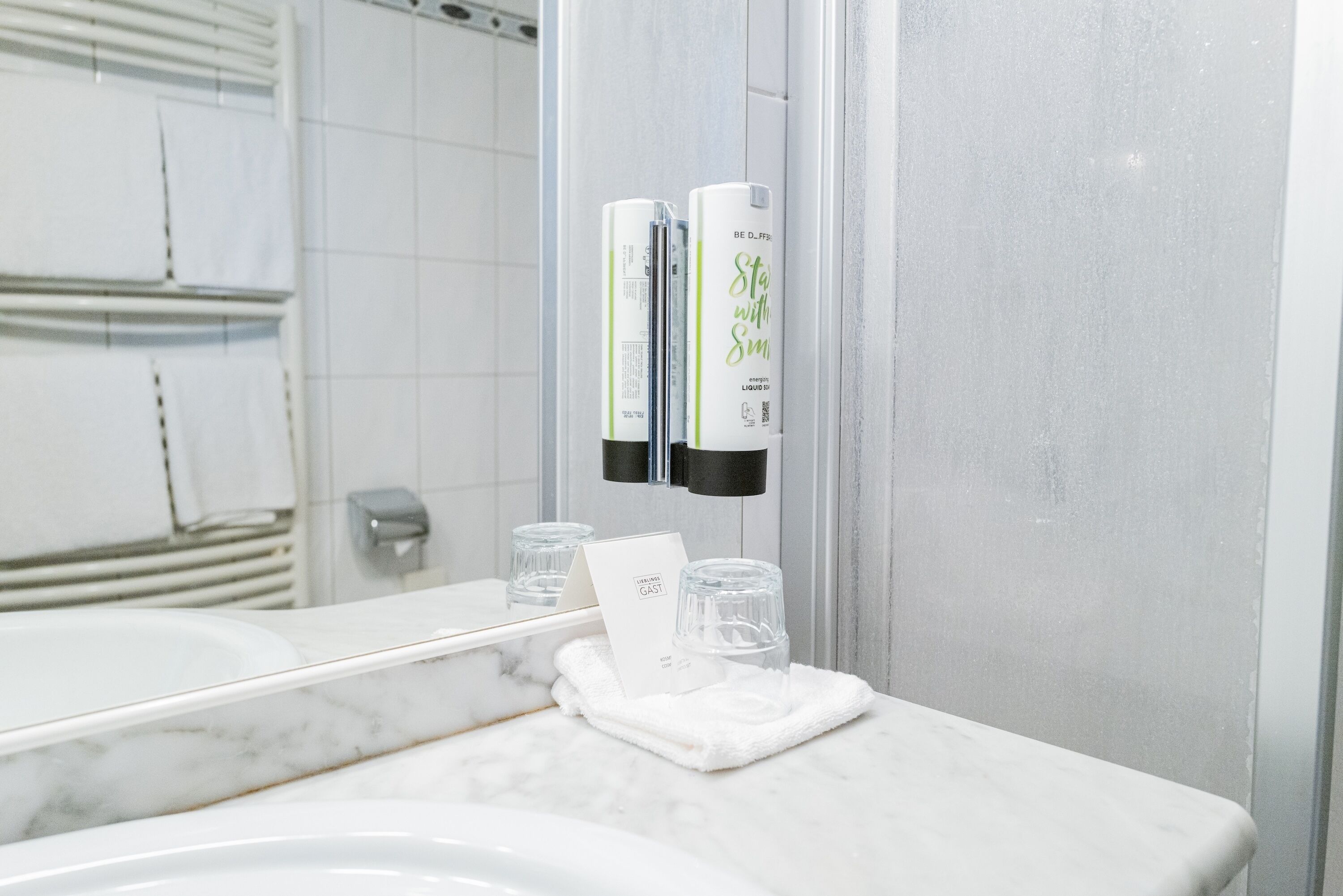 A bathroom with a white marble sink, a mirror, and two hand sanitizer dispensers mounted on the wall.