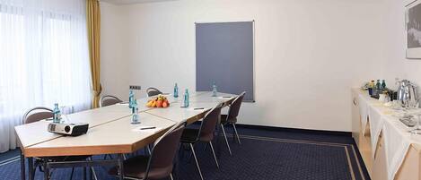 Una sala de conferencias con una larga mesa, sillas, un proyector, botellas de agua y una pizarra.