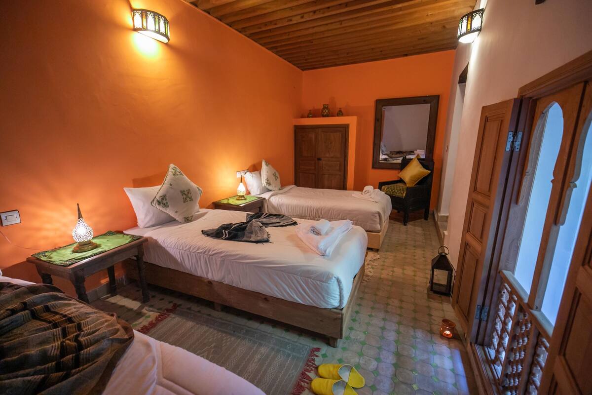 A hotel room with two beds, a nightstand with a lamp, a wooden door, and a patterned floor.