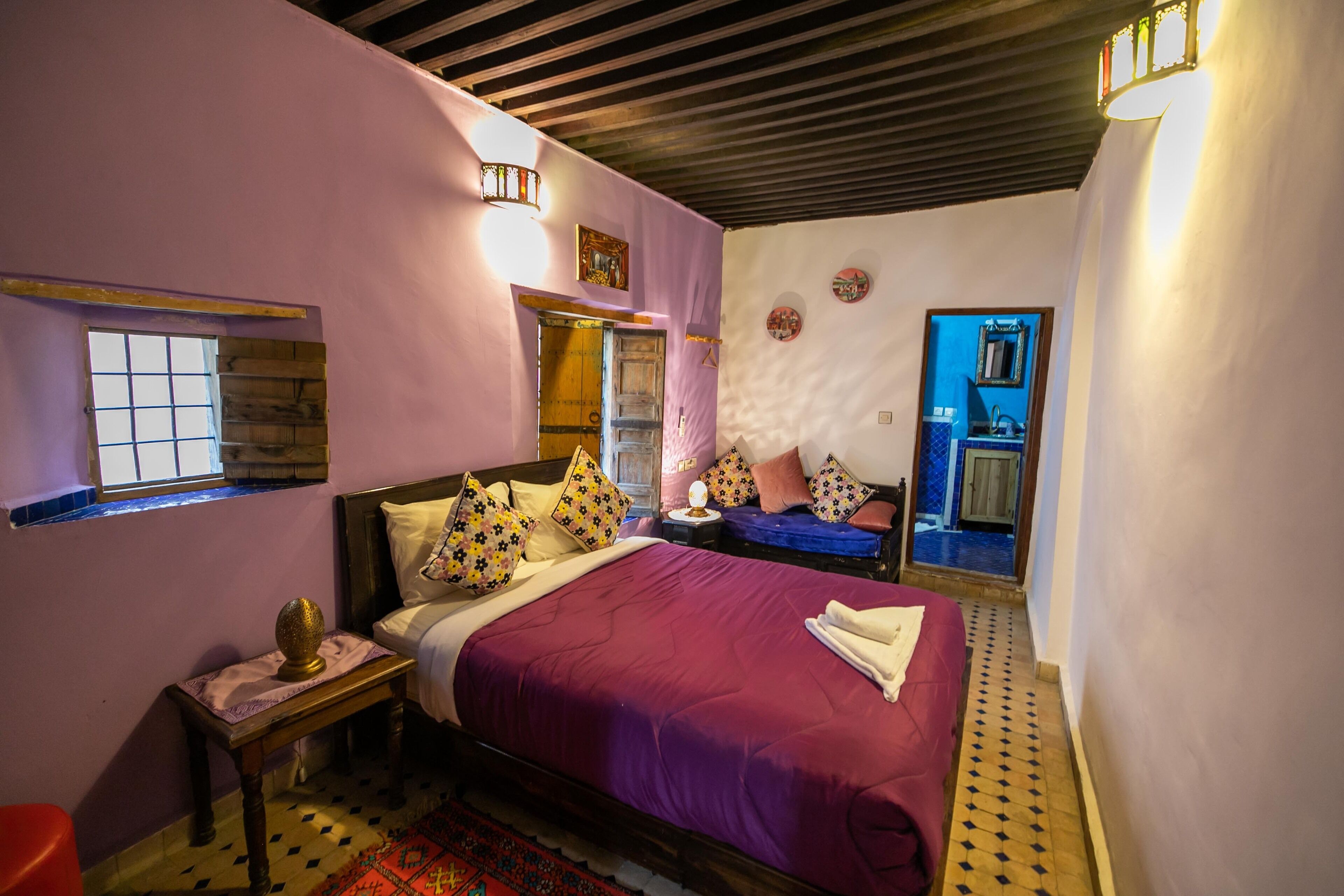 Une chambre à coucher avec un grand lit, une table de chevet, une lampe et une fenêtre donnant sur l’extérieur.