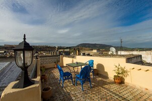 Una terraza en la azotea con una mesa y sillas, plantas en macetas y vistas a la calle.