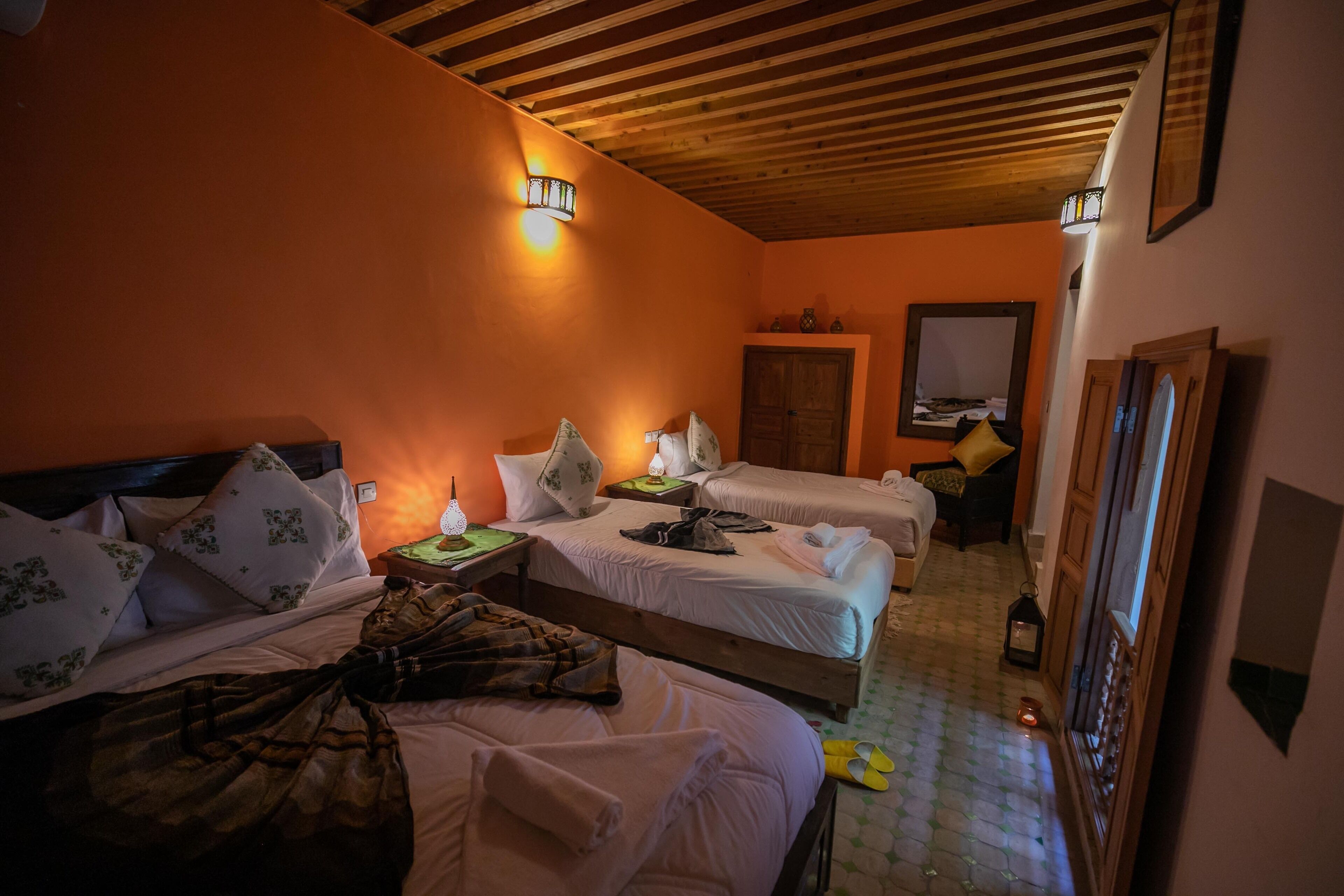 A hotel room with two beds, wooden headboard, orange walls, and a tiled floor.
