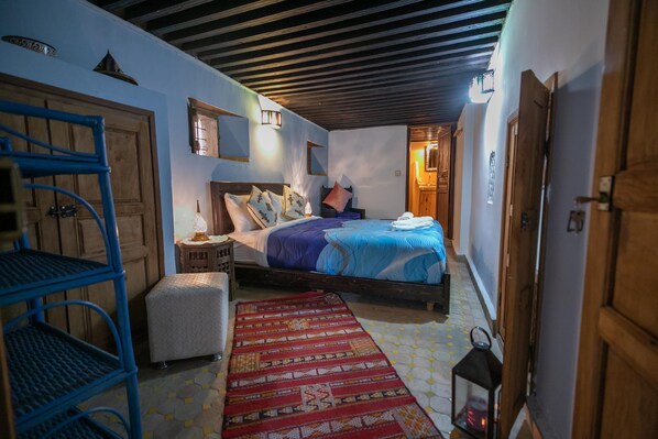 A bedroom with a wooden bed, a blue metal shelf, a patterned rug, and a nightstand with a lamp. - Riad Hidaya (Fes)