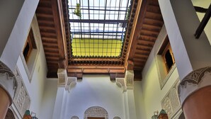 A traditional interior with a high ceiling, ornate wooden columns, and a patterned floor. - Riad Hidaya (Fes)