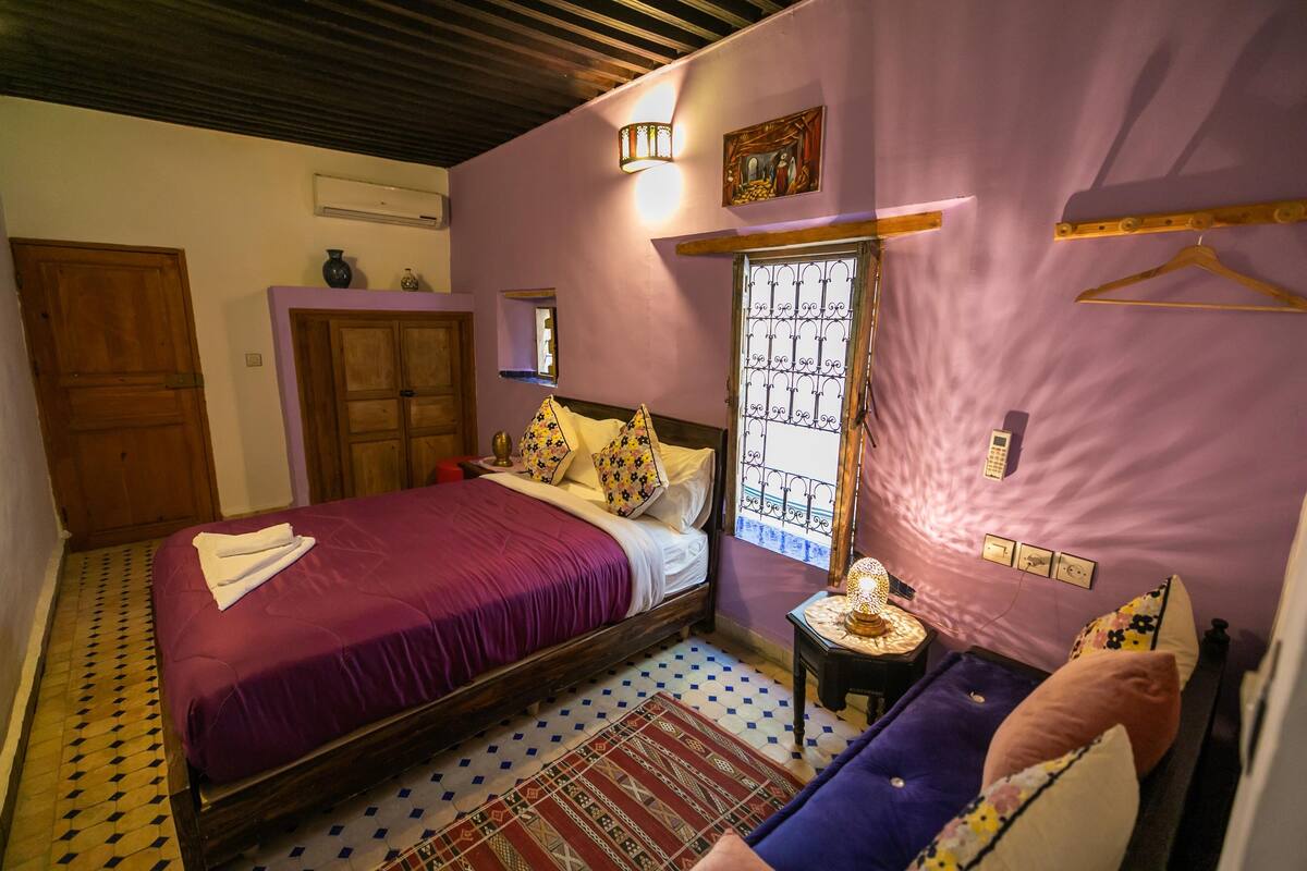 A bedroom with a bed, a nightstand, a dresser, a window with bars, and a door.