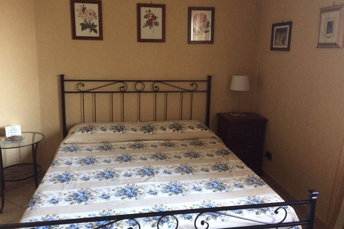 Una cama individual con colcha estampada, una mesita de noche con lámpara y tres cuadros en la pared.
