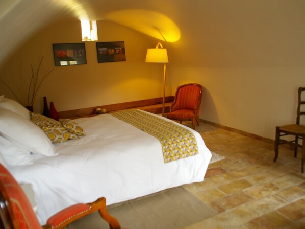 Un dormitorio con una cama grande, una silla, una lámpara y dos marcos de cuadros en la pared.