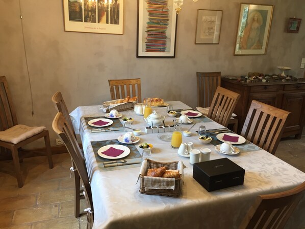 Mesa posta com itens de café da manhã, incluindo croissants, frutas e café.