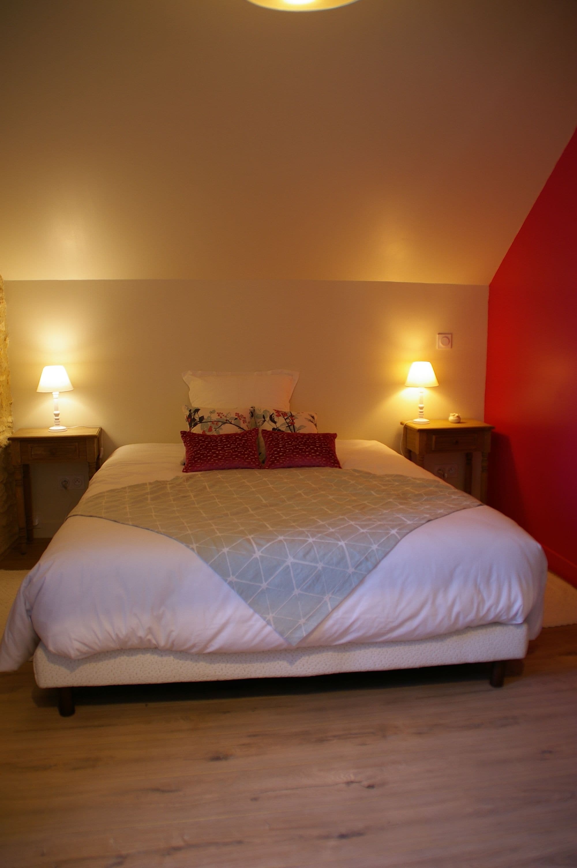 A neatly made bed with a geometric-patterned blanket, two bedside lamps, and a red accent wall.