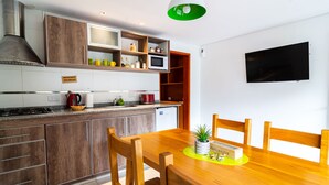 A modern kitchen with wooden cabinets, a built-in microwave, and a dining area with a wooden table and chairs. - Andino Aparts - El Chalten (El Chalten)
