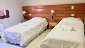 Habitación de hotel con dos camas individuales, cabecero de madera, lámparas de noche y una mesita pequeña.