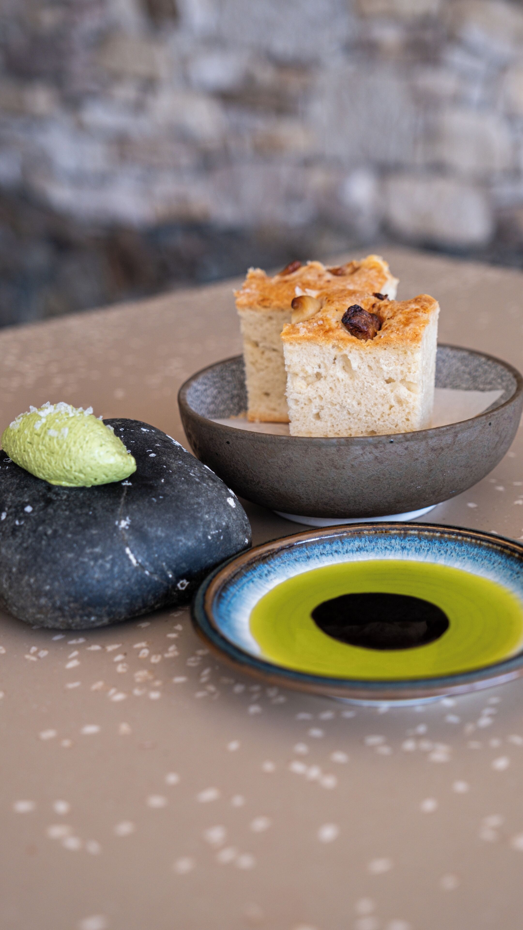 A dessert with a green garnish on a stone surface, a bowl with a slice of cake, and a small plate with a yellow rim.