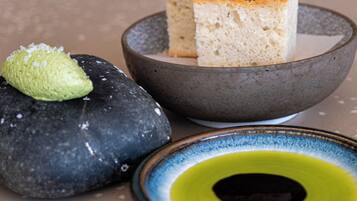 A dessert with a green garnish on a stone surface, a bowl with a slice of cake, and a small plate with a yellow rim.