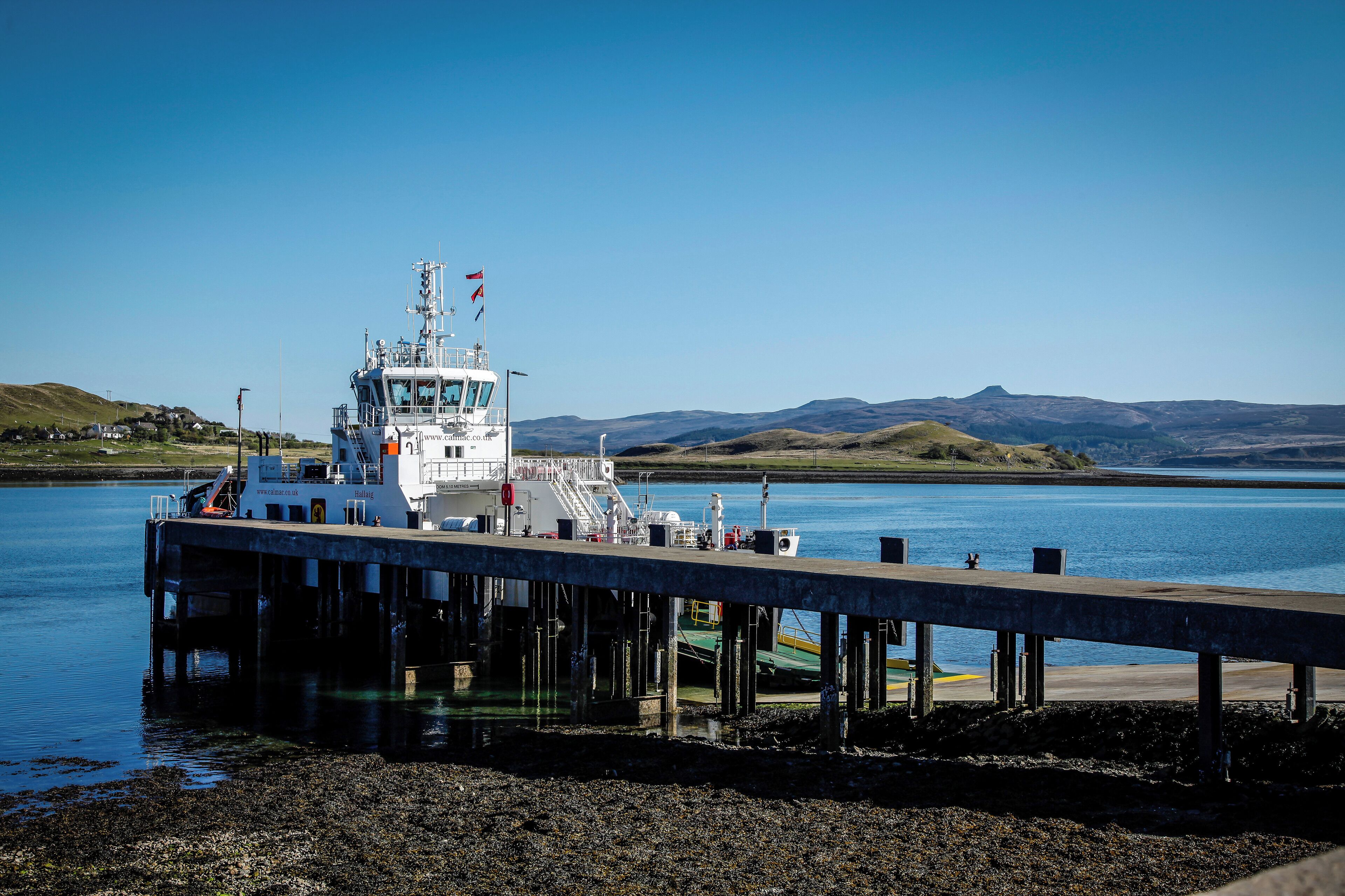 Un ferry atracado en un muelle, con vista despejada al agua y colinas distantes.