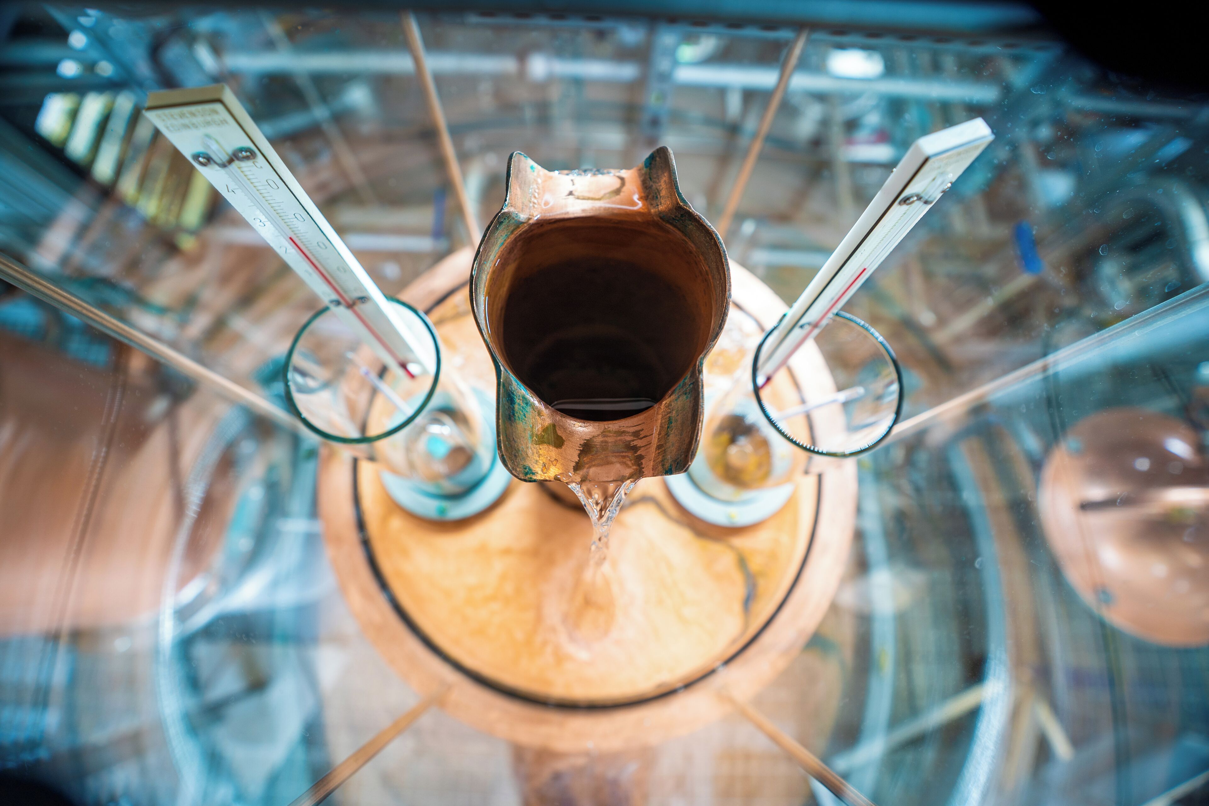 A top-down view of a copper kettle with a spout, surrounded by glassware.